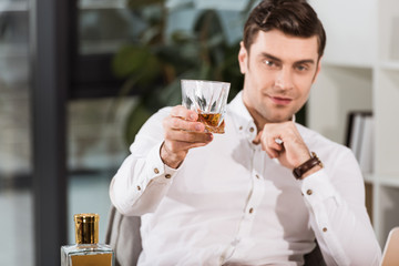 handsome businessman holding glass of whiskey and looking at camera at office