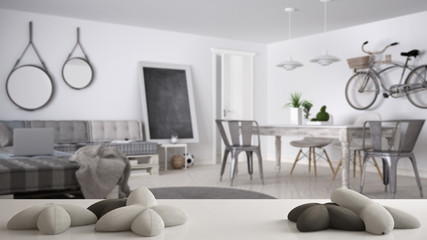 White table, desk or shelf with five soft white pillows in the shape of stars or flowers, over blurred modern scandinavian living room, minimal architecture interior design concept
