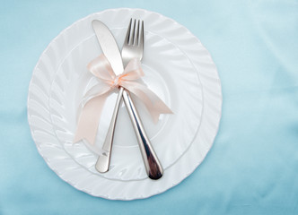 White plate, fork and knife on light background.