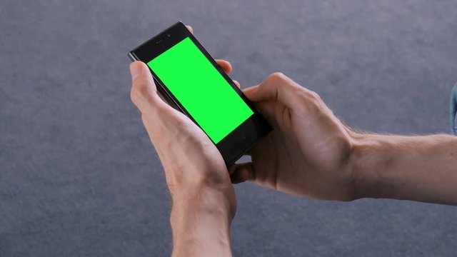 Man looking at smart phone phone with green screen. Close up shot of man hands with mobile phone. Chroma and technology concept