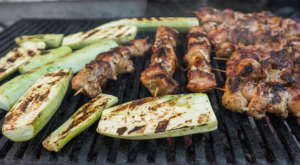 Zucchini and meat shish cooking on a grill.