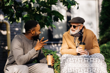 senior disabled man in wheelchair and african american man drinking coffee from paper cups and...