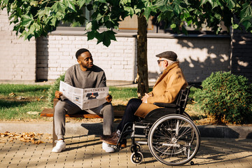 senior disabled man in wheelchair and african american man spending time together and reading...
