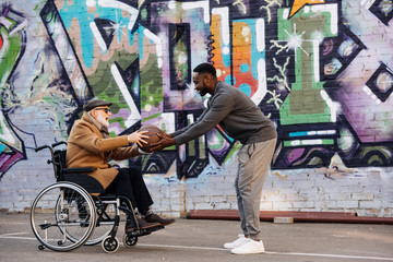 side view of senior disabled man in wheelchair and african american man playing basketball together...