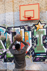 handsome african american man throwing basketball ball into ring on street