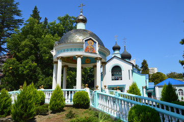 Fototapeta na wymiar Bright Christian chapel with a church on a dais with a staircase in a green garden in summer