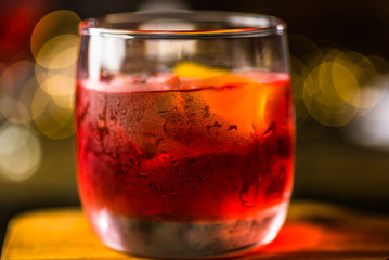 A red coloured cocktail with ice cubes and a twist of lemon 