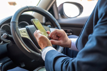 Businessman texting on smartphone inside car on bright day