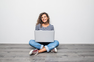 Portrait of satisfied woman with laptop on legs and sitting in lotus pose on the floor over grey wall