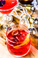 A red coloured cocktail with ice cubes and a twist of lemon 