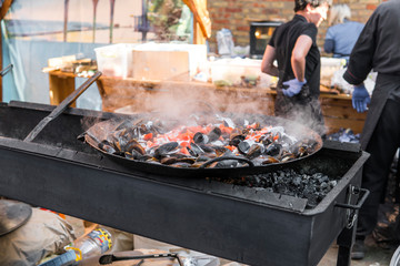 Fresh mussels at grill pan. Seafood barbecue outdoors. Picnic healthy food, mussels in shells. Plenty of mussel shells cooking at large metallic pan.