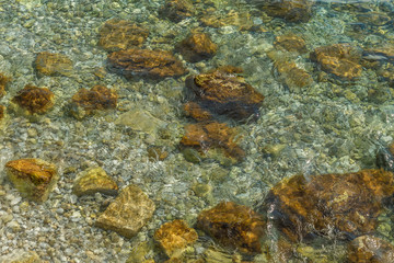 Naklejka na ściany i meble Sea water and pebbles on a summer day, glare and light blur