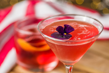 A red colored cocktail with a purple flower, with other cocktails in the background  