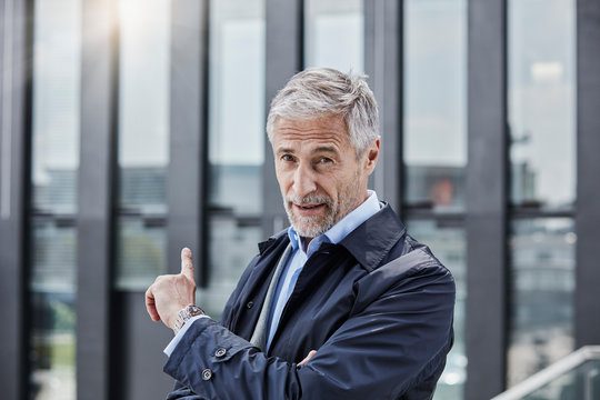 Germany, Duesseldorf, portrait of businessman pointing at office building at Media Harbor