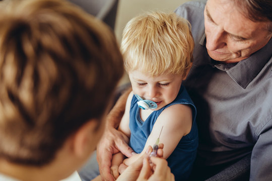 Father holding son while being vaccinated by pediatrician