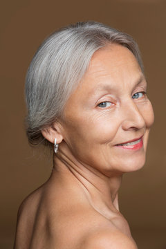 Portrait of naked senior woman with grey hair in front of brown background