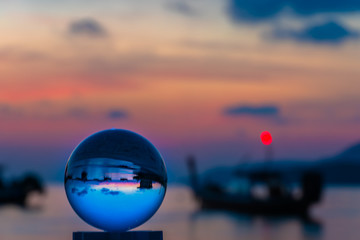 crystal glass ball sphere reveals sunrise seascape with spherical perspective on the beach in Phuket island.