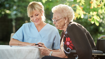 Pflegerin hilft Seniorin beim Kreuzworträtzeln