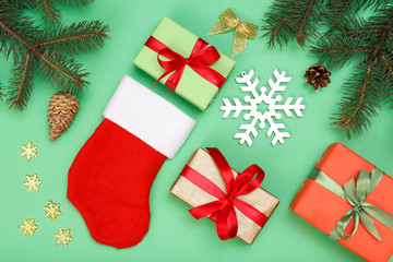 Santa's boot, gift boxes, fir tree branches with cones on green background