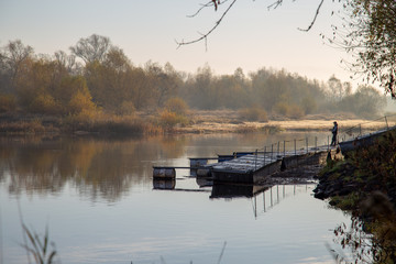 mężczyzna łowi ryby z pomostu nad rzeką o wschodzie słońca © Arkadiusz