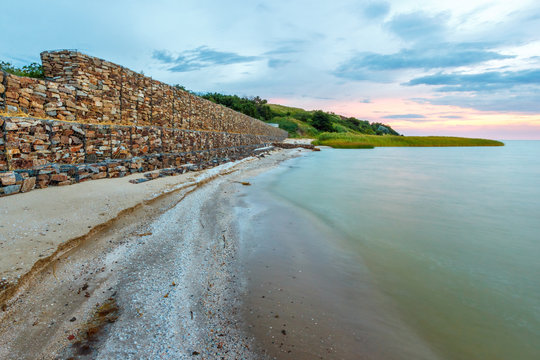 The twilight landscape with the breakwater wall of stones in the metal net on the seashore. Taganrog bay, Azov sea, Russia