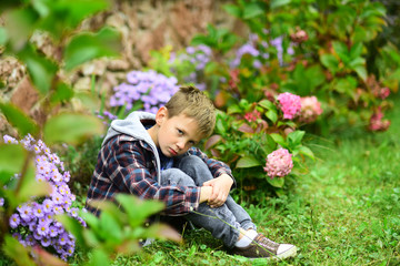Unhappy and miserable. Little boy in deep sorrow. Little boy with sad look hide in garden. Little...