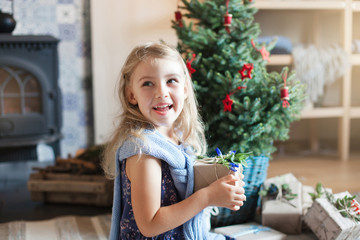 Happy child girl gets gift box under Christmas tree. Kid holds surprise. Natural children emotions....