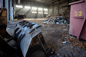 Heavy bulldozer bucket in rays of evening sun in building of waste recycling plant moves tons of...