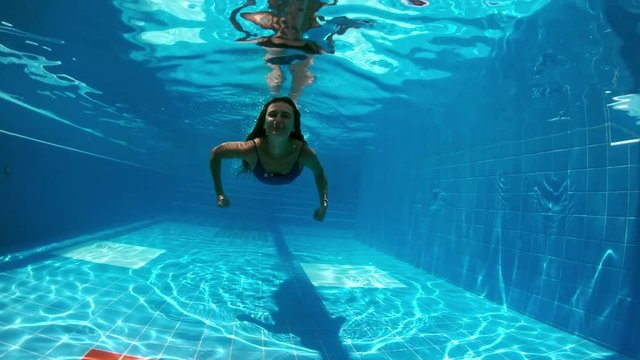Young lady swimming underwater in the pool. Underwater woman portrait in swimming pool