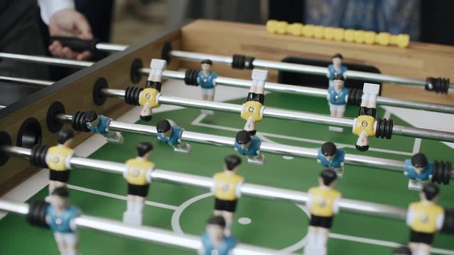 Friends having fun together playing foosball. Colleagues playing table football on break. Office people enjoying table soccer game. Close up of table football kicker game, 4k, handheld