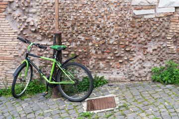 The Bicycle is chained to a lamppost at a brick wall.