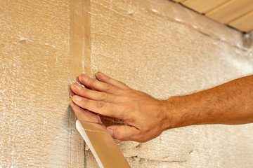 Male hands using aluminum tape to glue the joint foil insulation for the walls of the sauna.