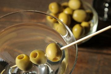 Martini in a glass wineglass with green olives on a skewer on a brown wooden table. cocktails. bar