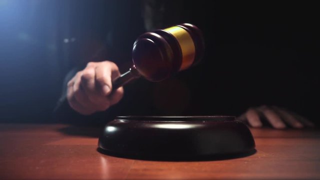 Judge hitting Gavel off a block in courtroom, dark background slow motion dolly shot