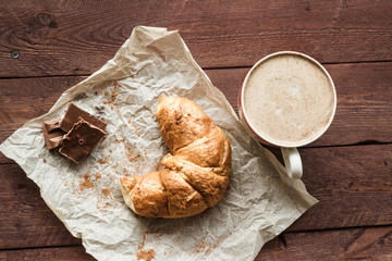 Tasty croissants with cup of coffee and chocolate on wooden table