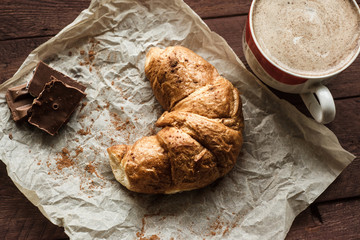 Tasty croissants with cup of coffee and chocolate on wooden table
