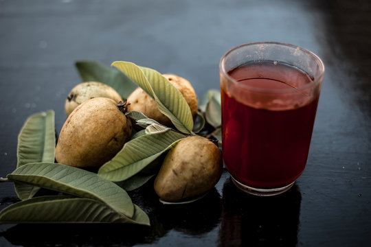 Close up of organic juice of red guava or amarood or jamrukh in a transparent glass with raw guava and its leaves on wooden surface.