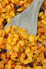 Organic golden raisins on a wood spoon.