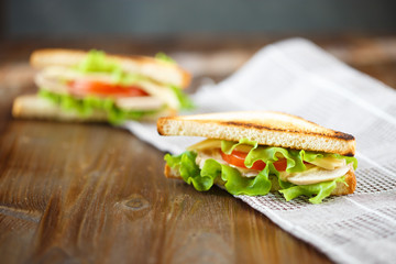 Appetizing sandwich with chicken, tomatoes, lettuce, cheese on a wooden plate on a dark background
