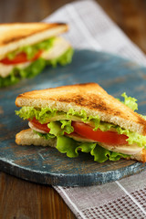 Two tasty sandwich with chicken, tomatoes, lettuce, cheese on a wooden plate on a dark background