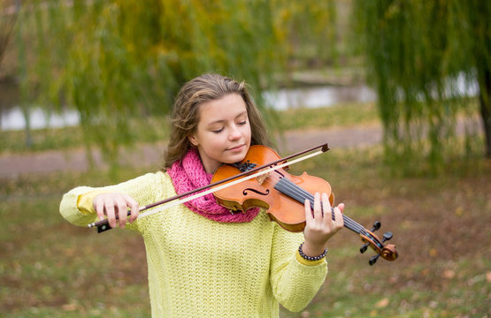 Girl playing the violin eyes closed in the autumn park at a lake and willow foliage background.