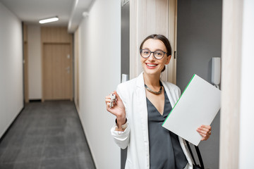 Portrait of an excited woman with key and documents standing near the dooor of the new apartment in the walkhall