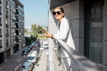 Young business woman in white suit and sunglasses on the balcony of the apartment in the modern residential area