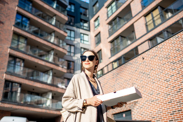 Fototapeta premium Young stylish woman walking with pizza box outdoors at the modern residential area