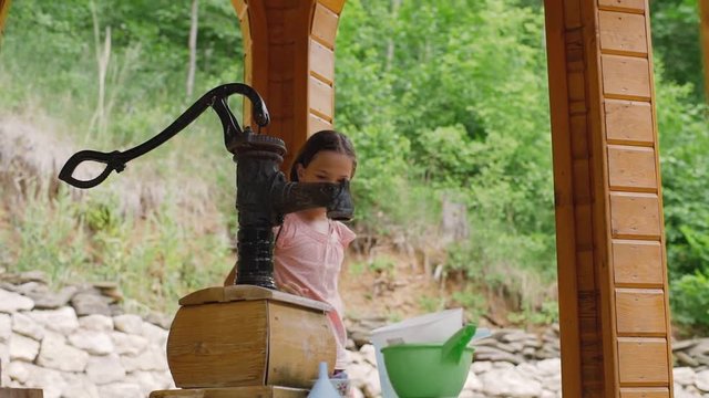 A young girl draws water from a water inlet column. The girl shakes the water.