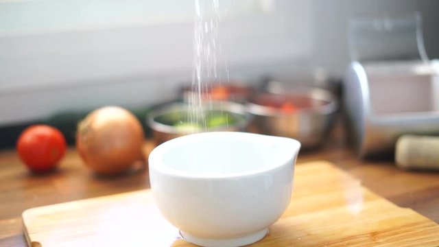 Woman adding salt or spices into bowl in kitchen