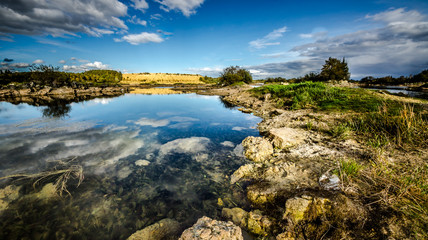 Sandy hills. Lake in the Sandy canyon. Warm colors background. Yellow sandstone textured mountain, white thin sand dune, bright sky. Sunshine landscape