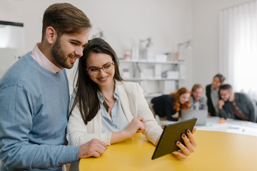 Two people taking selfie with their colleagues solving problems in the background