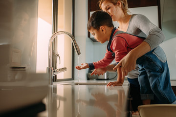 Little boy with mother washing hands in kitchen sink - Powered by Adobe