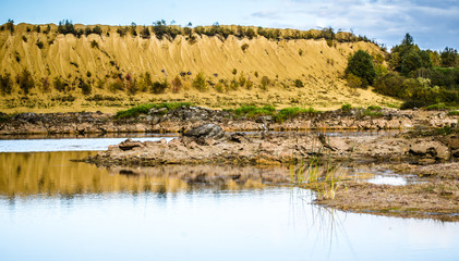 Sandy hills. Lake in the Sandy canyon. Warm colors background. Yellow sandstone textured mountain, white thin sand dune, bright sky. Sunshine landscape